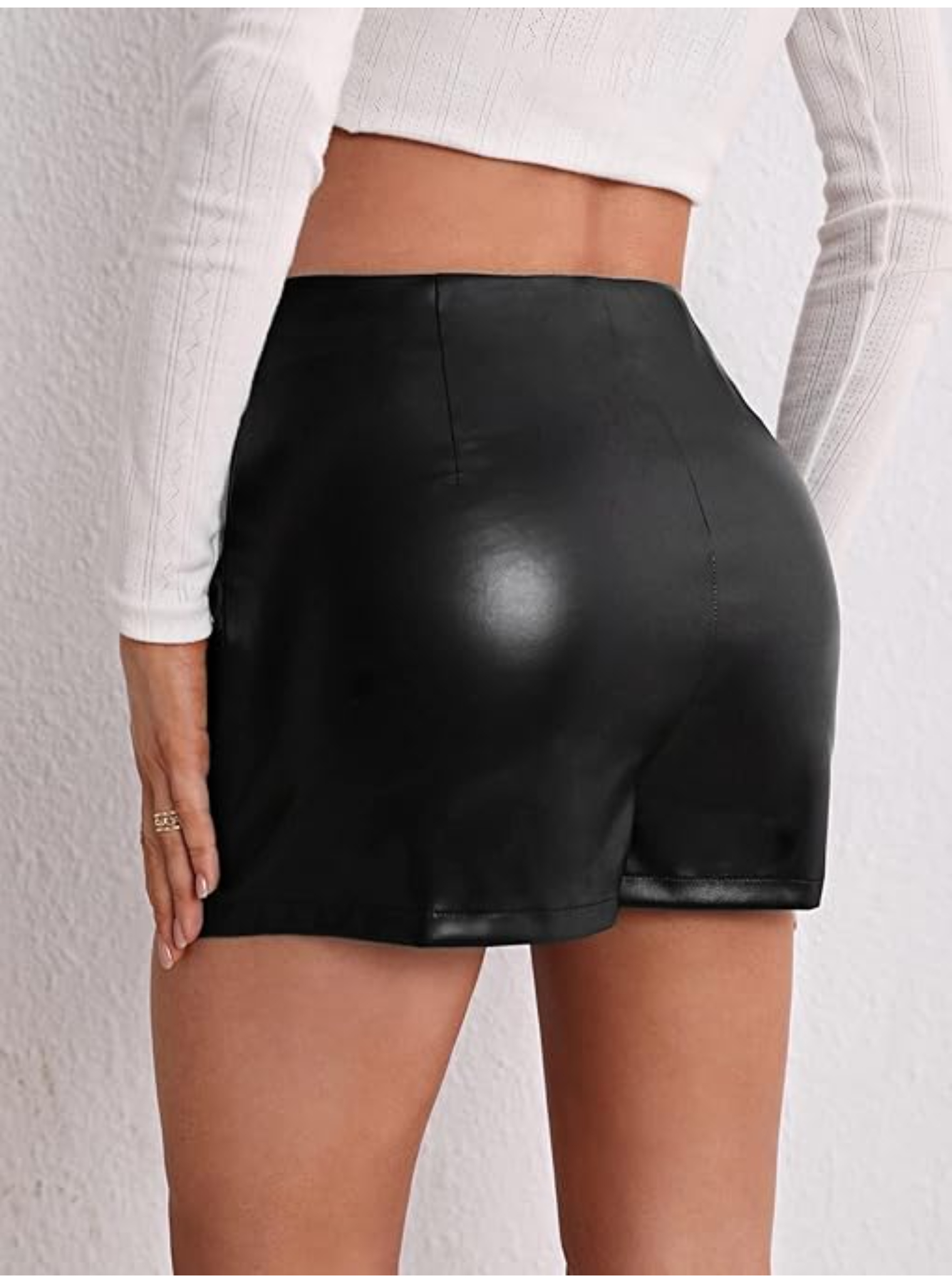 Vista trasera de mujer con short falda de cuero sintético negro, mostrando la cintura alta y el ajuste ceñido.