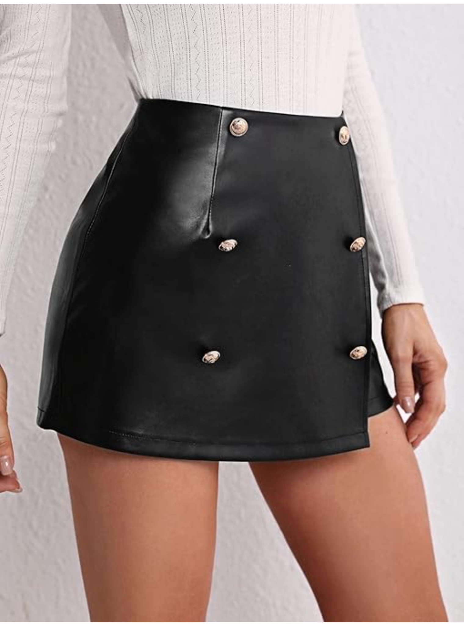 Vista lateral de short falda de cuero sintético negro, destacando el diseño cruzado y los botones dorados.