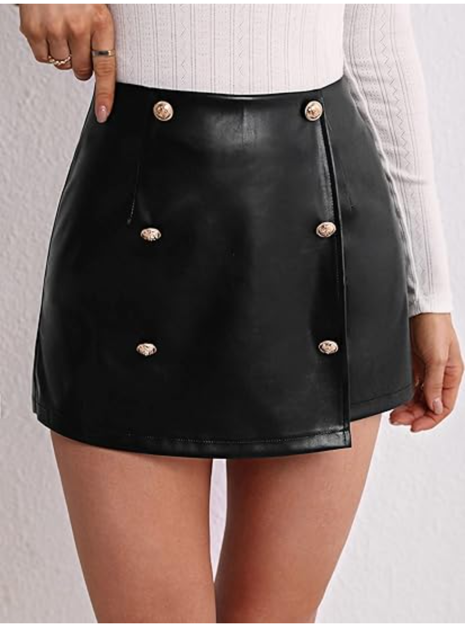 Vista frontal de short falda de cuero sintético negro con botones decorativos dorados, combinado con un top blanco.
